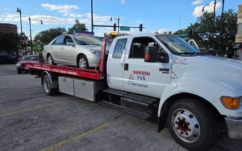 KVS flatbed carrying a sedan through a Chicago intersection
