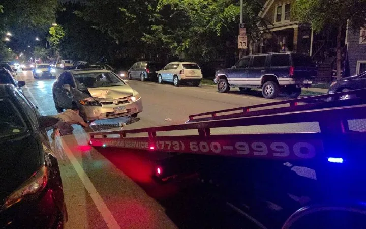Night collision recovery on a Chicago residential street, damaged sedan and running lights