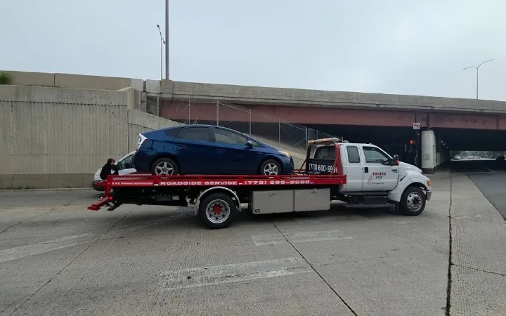 Blue Toyota Prius loaded on the KVS flatbed under a Chicago expressway viaduct