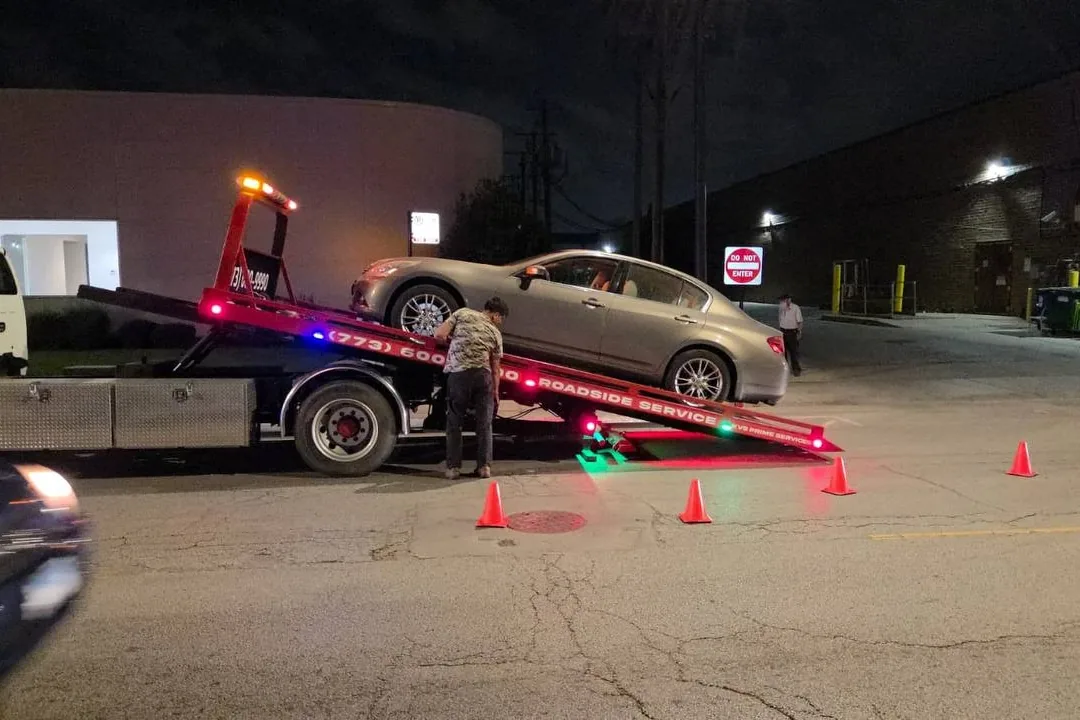 KVS operator loading a sedan onto a lit flatbed at night with cones set out around the work area