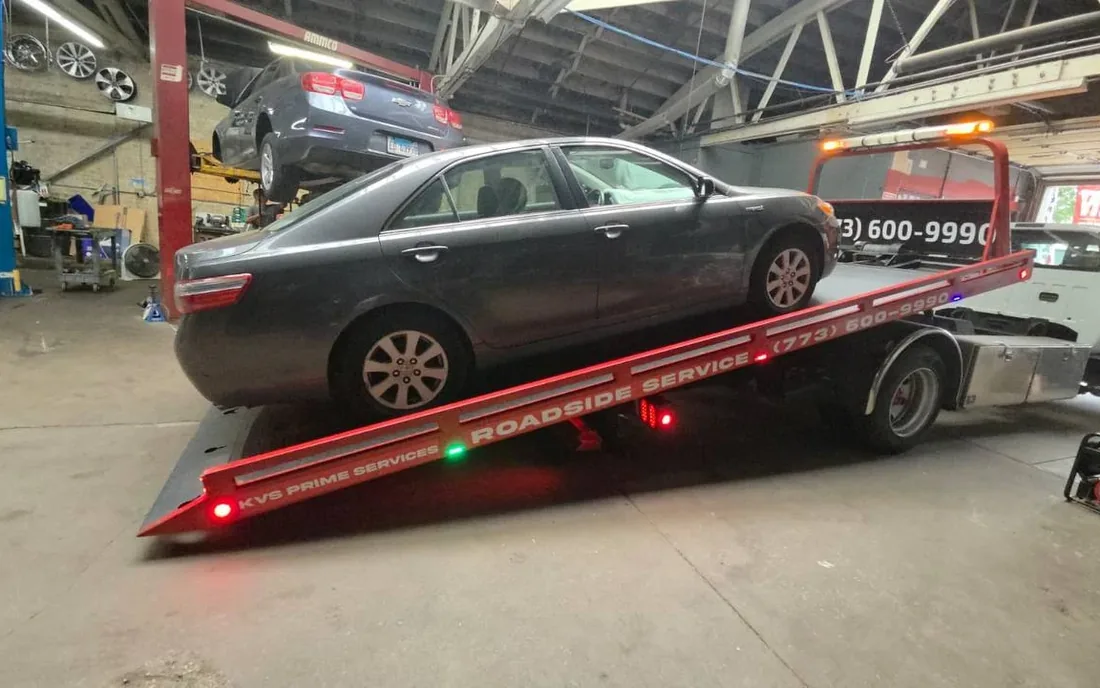 Toyota Camry being unloaded from the KVS flatbed inside a repair shop