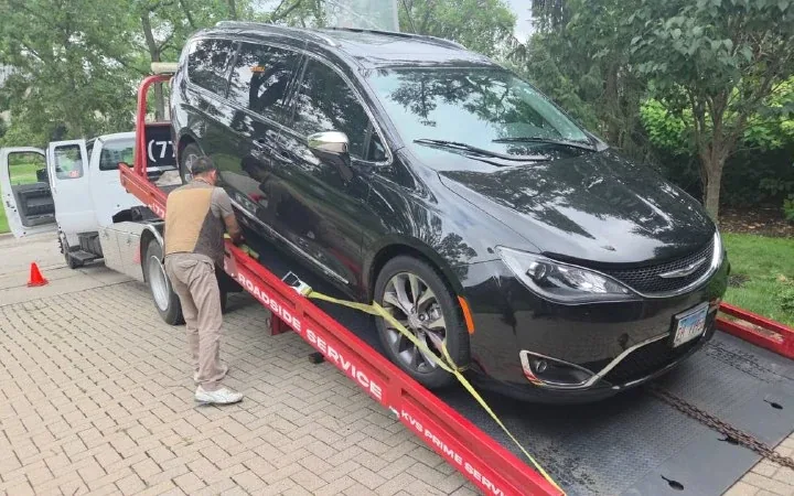 KVS operator ratcheting wheel straps over the tyres of a minivan on the flatbed